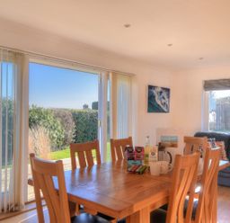 A dining area with a wooden table and chairs next to sliding glass doors with a view of a garden at Pendower in Charmouth
