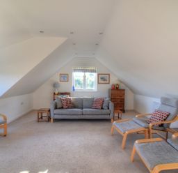 An attic living room with a sofa armchairs footstools side tables and a chest of drawers at Pendower in Charmouth