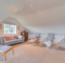 A sitting room with a sofa, armchairs, ottomans, a window, a chest of drawers, a lamp, and framed pictures at Pendower in Charmouth