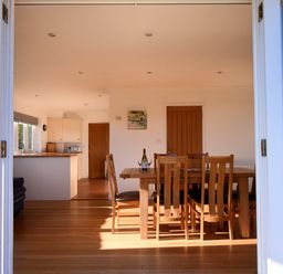 A dining area with wooden table and chairs and kitchen in the background at Pendower in Charmouth