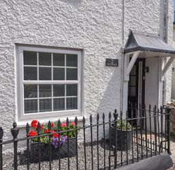 The front entrance of a white textured wall house with a window, flower boxes, and a black iron fence at Nutwood in Charmouth
