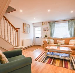 A living room with a green armchair a beige sofa a wooden coffee table and a striped rug at Nutwood in Charmouth