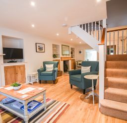 A living room with two blue armchairs a wooden coffee table a fireplace a TV and carpeted stairs at Nutwood in Charmouth
