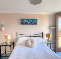 A bedroom with a double bed two bedside tables with lamps wall shelves and a balcony door at 9 Maritime House in West Bay