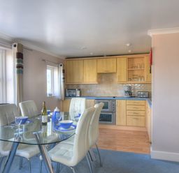 A kitchen with wooden cabinets glass dining table white chairs and blue dining set at 9 Maritime House in West Bay