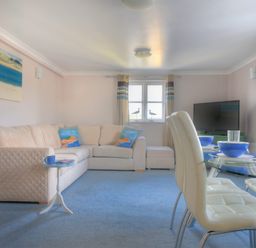 A living room with a beige sectional sofa and a round glass dining table with white chairs at 9 Maritime House in West Bay