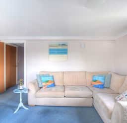 A living room with beige sofa blue carpet small round blue table and a painting on the wall at 9 Maritime House in West Bay