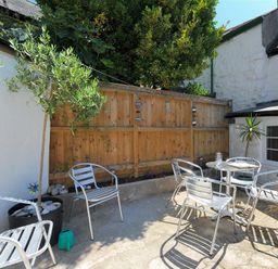 An outdoor patio with metal chairs and a table near a wooden fence and white building at Monmouth Cottage in Lyme Regis