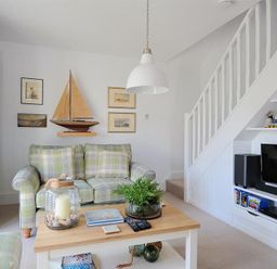 A living room with a plaid sofa a wooden coffee table decorative sailboat wall art and a television under stairs at Highpoint Lodge Lyme Regis