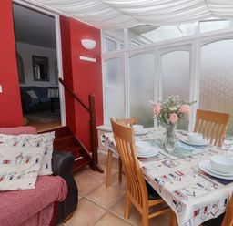 A dining area with a table set for four with a flower vase and wooden chairs next to a red wall with an armchair and stairs at Bay View in Lyme Regis