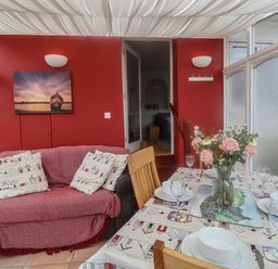 A dining area with a table set for four and a sofa with cushions against a red wall at Bay View in Lyme Regis