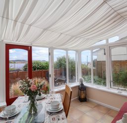 A dining area with a table set and flowers with windows and a red door at Bay View in Lyme Regis