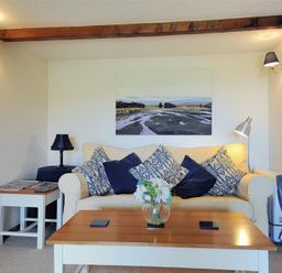 A living room with a beige sofa with blue and patterned cushions a wooden coffee table with a vase of flowers and a side table with a lamp at Willows in Charmouth