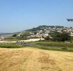 A view of a coastal village with houses on a hillside and a grassy field in the foreground at Willows in Charmouth
