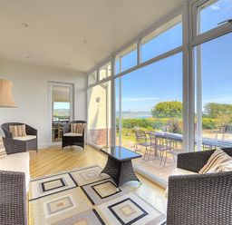 A sunroom with wicker chairs and a patterned rug overlooking a patio with a table and chairs at Somerhill in Lyme Regis