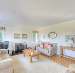 A living room with two beige sofas a wooden coffee table a wooden side table a fireplace and two windows at Somerhill in Lyme Regis
