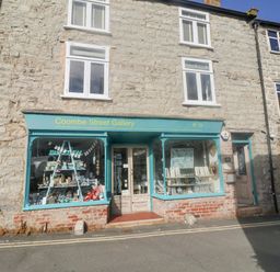 Stone building with two upper windows and a gallery shop with turquoise window frames and door at Coombe Street Gallery in Lyme Regis