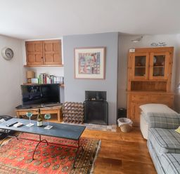 A living room with a sofa a coffee table wine glasses a TV and a wooden cabinet at Coombe Street Cottage Lyme Regis