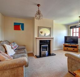 A living room with two sofas a fireplace a television and two chandeliers at 28 Barnes Meadow in Uplyme