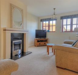 A living room with a sofa a fireplace a television on a wooden stand and two windows at 28 Barnes Meadow in Uplyme