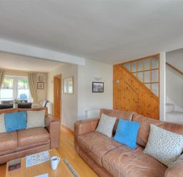 A living room with leather sofas and cushions next to a wooden staircase at Ivy Cottage in Beer