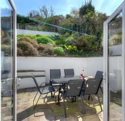 A patio with a glass table and six black chairs with a garden on a slope behind at Ivy Cottage in Beer