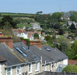 Roofs and chimneys of stone houses with a hillside and more houses in the background at Ivy Cottage in Beer