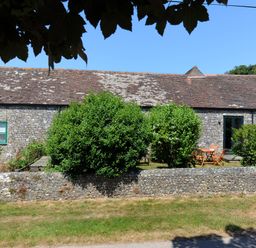 A stone building with green windows and a brown tiled roof behind green bushes and a low stone wall at 3 Home Farm South in Rousdon