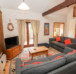 A living room with two gray sofas with red pillows a wooden coffee table a television on a wooden stand and French doors at 3 Home Farm South in Rousdon