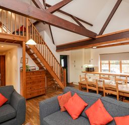 A living room with gray sofas and red cushions a wooden dining table and chairs wooden staircase and exposed beams at 3 Home Farm South in Rousdon