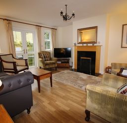 A living room with armchairs a sofa a coffee table a fireplace a television and double doors at Vine Cottage in Charmouth