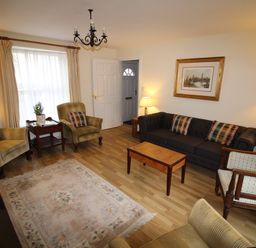 A living room with armchairs a sofa a wooden coffee table a rug a side table with a plant and a framed picture on the wall at Vine Cottage in Charmouth