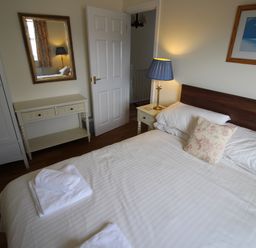 A bedroom with a double bed with white linens a bedside table with a lamp a mirror above a console table and a framed picture on the wall at Vine Cottage in Charmouth