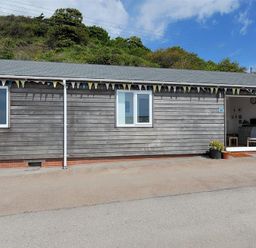 A wooden single-story house with two windows and an open door with bunting above at The Beach Hut in Lyme Regis