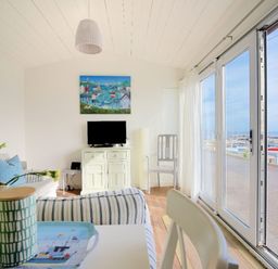A living area with striped sofas a television on a cabinet and large sliding glass doors overlooking a marina at The Beach Hut in Lyme Regis