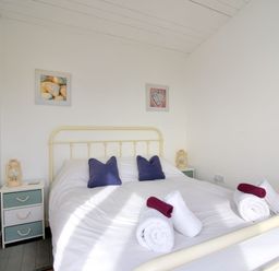 A bedroom with a bed with white bedding and blue pillows and nightstands with lamps at The Beach Hut in Lyme Regis
