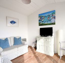 A living room with a striped sofa and blue cushions a cabinet with a television and two paintings on the walls at The Beach Hut in Lyme Regis