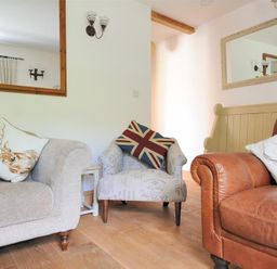 A living room with a beige sofa a patterned armchair with a union jack cushion and a brown leather sofa with animal print cushions at Bethel Cottage in Lyme Regis