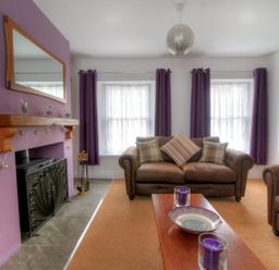 A living room with leather sofas a wooden coffee table with candles a fireplace with a mirror above and purple curtains at Sunnyside in Colyton