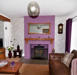 A living room with a purple accent wall a wood-burning stove a brown sofa and a wooden coffee table at Sunnyside Colyton