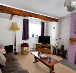A living room with a brown leather sofa wooden coffee table and a television on a stand at Sunnyside in Colyton