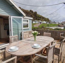An outdoor wooden deck with a dining table and chairs set with bowls glasses and flowers at Ammonite Lyme Regis