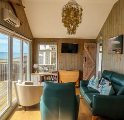 A sitting room with green sofas and a white armchair facing a television and sliding glass doors showing a sea view at Ammonite in Lyme Regis