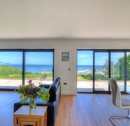 A living room with glass doors overlooking the sea and a table with flowers at Harbour Heights Cottage Lyme Regis