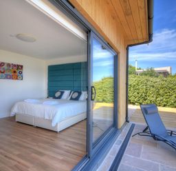 A bedroom with a double bed and towels on it next to a sliding glass door opening to an outdoor patio with a blue lounge chair at Harbour Heights Cottage in Lyme Regis