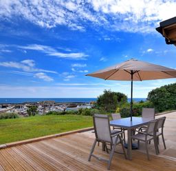 An outdoor patio with table chairs and umbrella overlooking a marina and sea at Harbour Heights Cottage in Lyme Regis