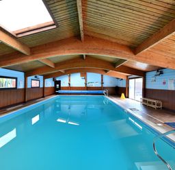 An indoor swimming pool with wooden ceiling beams and blue walls at 4 Pinewood Retreat in Pinewood