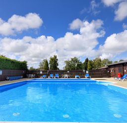 An outdoor swimming pool with blue water surrounded by lounge chairs tables and a wooden fence at 4 Pinewood Retreat in Pinewood