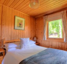 A bedroom with wooden walls and ceiling a bed with white sheets two bedside tables with lamps and a window with curtains at 4 Pinewood Retreat in Pinewood