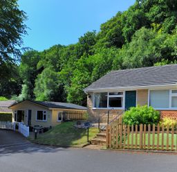 A residential street with one house and a small building surrounded by trees at 36 Fernhill Heights in Charmouth